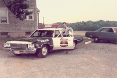 a Monroe Township Police Officer standing next to what is believed to be a 1974 Plymouth Fury police car in the parking lot of the Police Station on Spotswood Englishtown Road